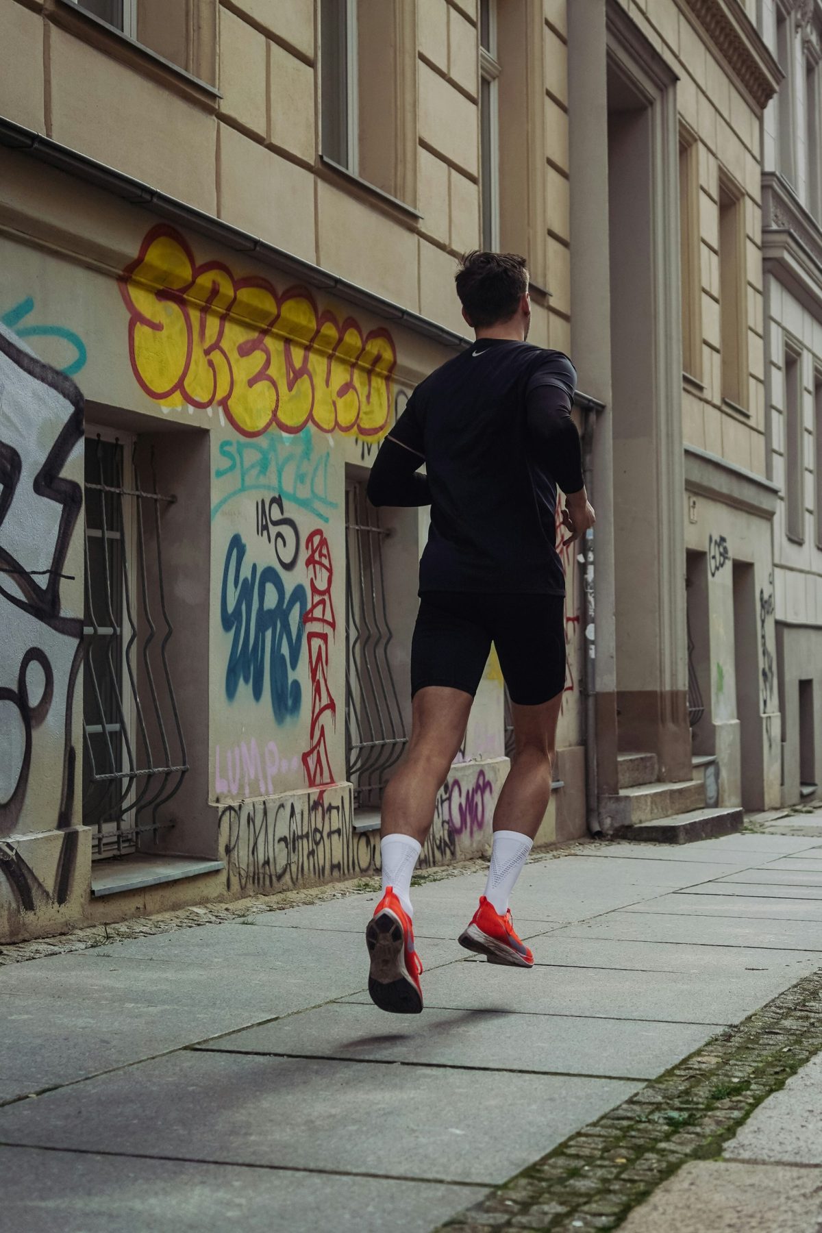 homme en short et t-shirt noirs faisant son jogging sur le trottoir